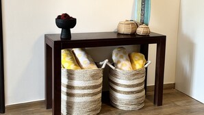 A wooden console table with two woven baskets underneath, a mirror with a wooden frame, and a surfboard with a 'WELCOME' sign. - BEST DEAL IN HEART OF TAMARINDO. Block from the beach, walk to everything! (Tamarindo)