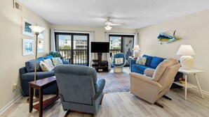A spacious living room with a large flat-screen TV, two sofas, a chair, and a ceiling fan. - SPRING/SUMMER DATES AVAILABLE (Orange Beach)