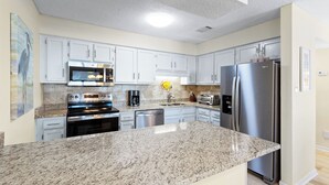A modern kitchen with granite countertops, stainless steel appliances, and white cabinetry. - SPRING/SUMMER DATES AVAILABLE (Orange Beach)