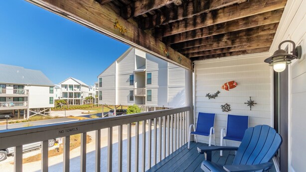 A wooden deck with blue chairs and a table, overlooking a beach with white buildings. - SPRING/SUMMER DATES AVAILABLE (Orange Beach)