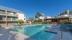 A swimming pool with lounge chairs, a covered seating area, and modern buildings in the background. - SPRING/SUMMER DATES AVAILABLE (Orange Beach)