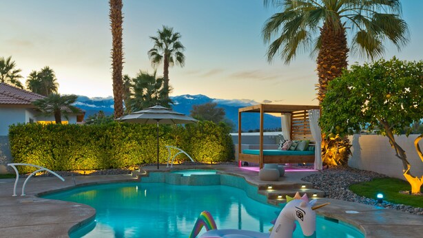 A swimming pool with a unicorn float, palm trees, and a view of mountains. - Great solar-powered house with pool/spa! (Palm Desert)