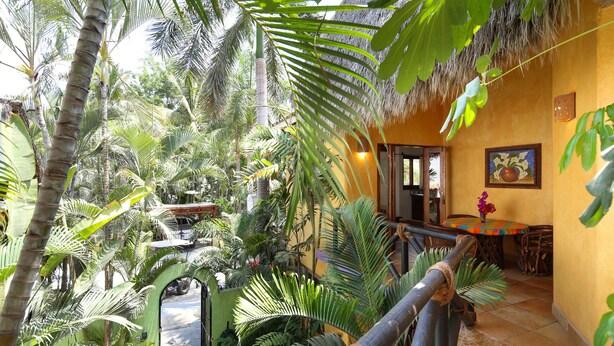 Un exuberante jardín interior con techo de paja, un área de comedor con mantel de colores y vistas a la vegetación circundante.
