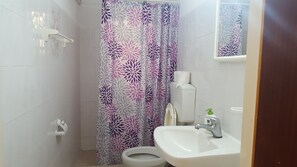 A bathroom with a shower curtain, toilet, sink, and a mirror above the sink. - Pizania (Kalymnos)