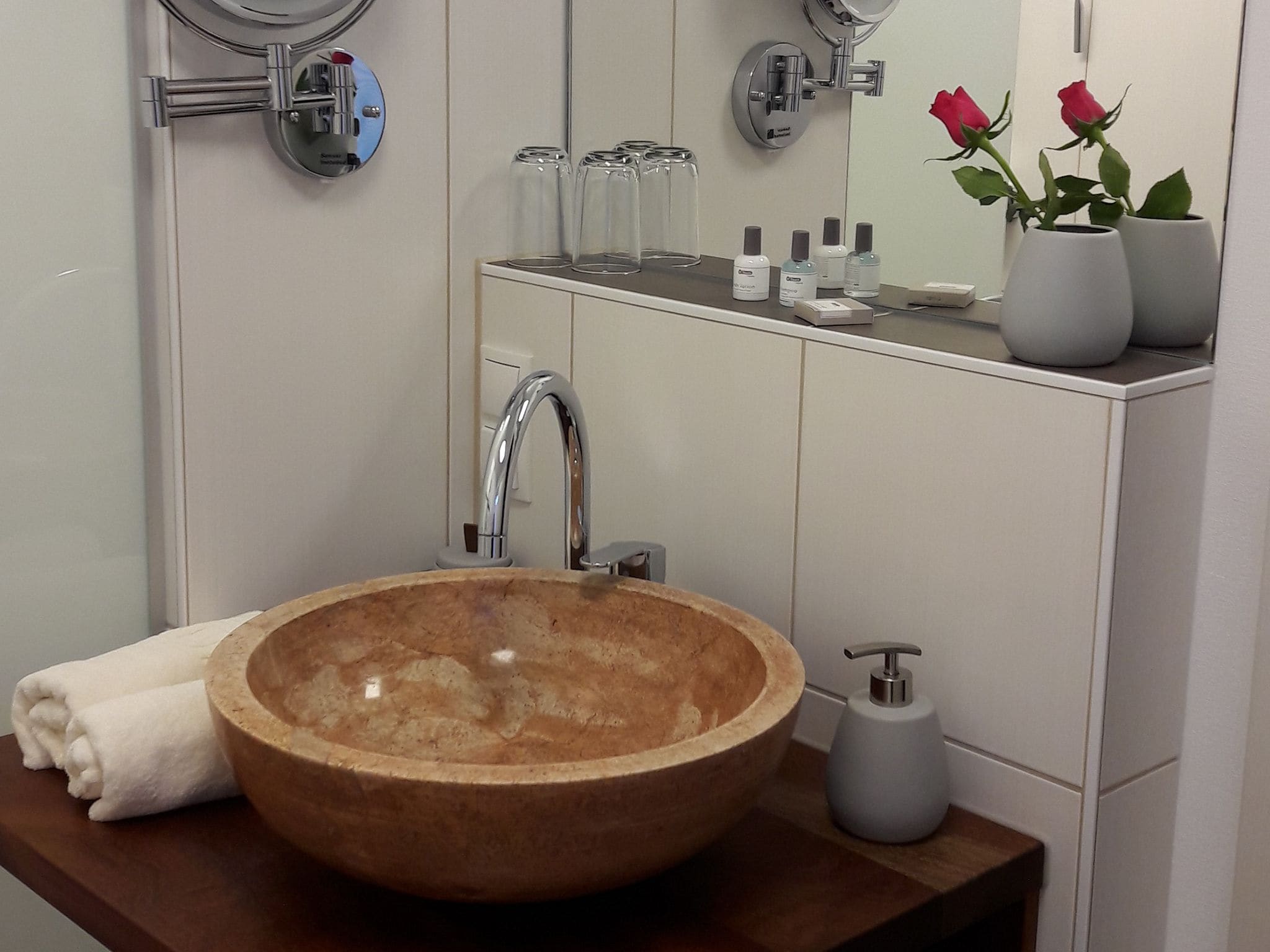 Une salle de bain avec un lavabo en forme de bol en bois, un miroir et un meuble-lavabo contenant des articles de toilette.