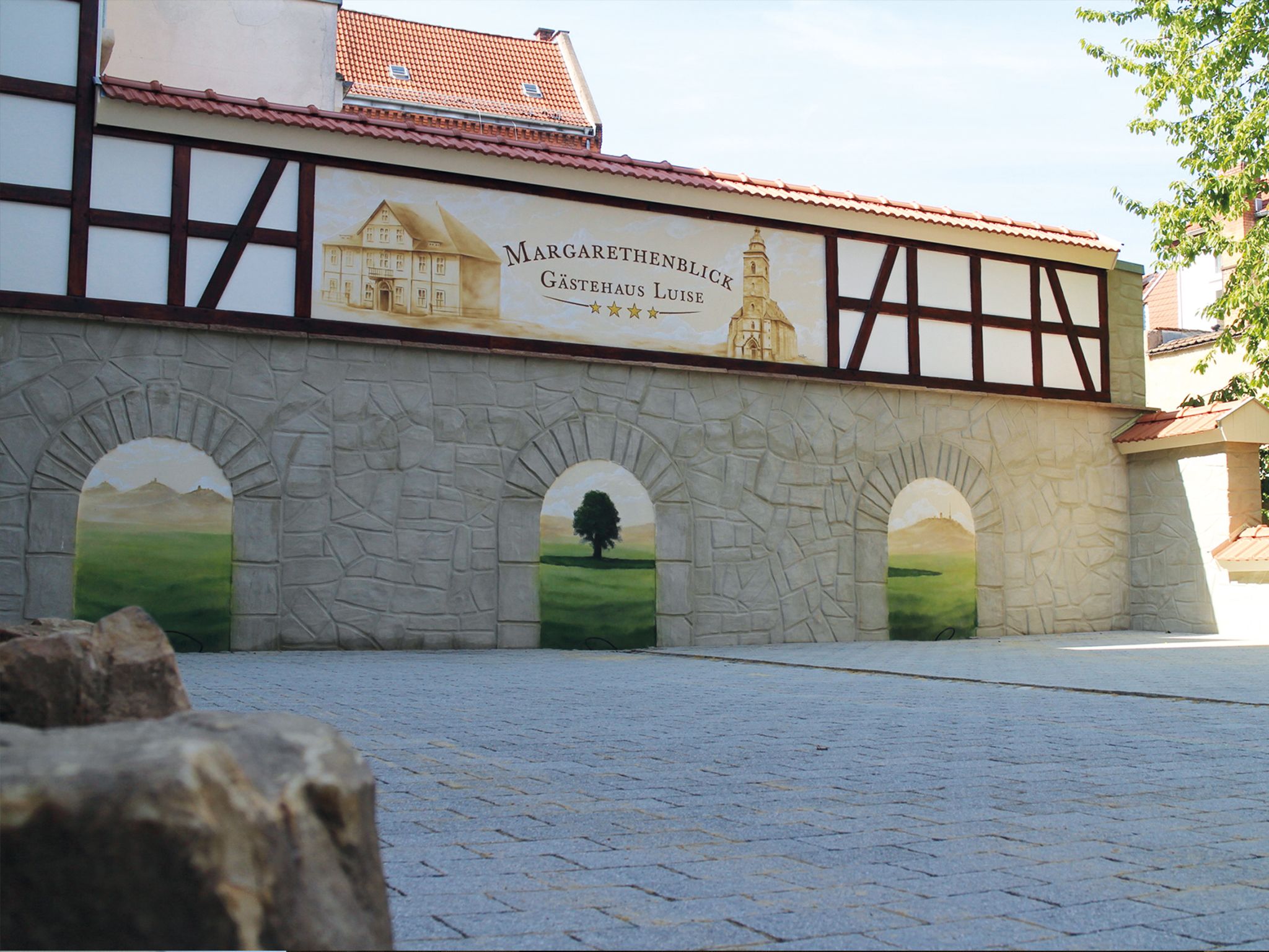 A building with a sign reading "Margarethenblick Gastehaus Luise" and three arched windows with landscape paintings.