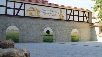 A building with a sign reading "Margarethenblick Gastehaus Luise" and three arched windows with landscape paintings.