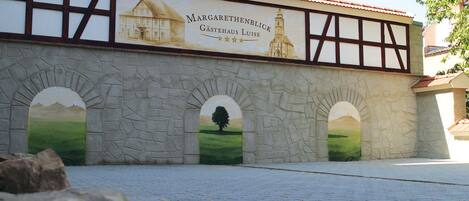 A building with a sign reading "Margarethenblick Gastehaus Luise" and three arched windows with landscape paintings.