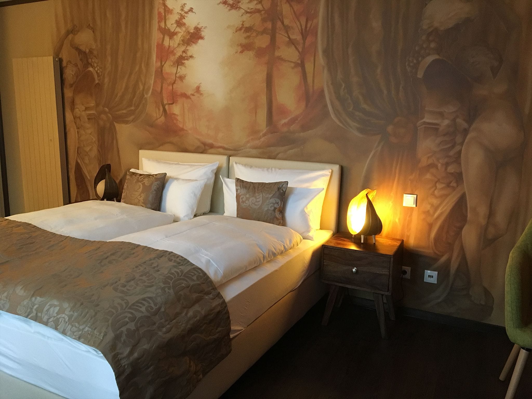 A double bed with a headboard, a bedside table with a lamp, and a mural on the wall.