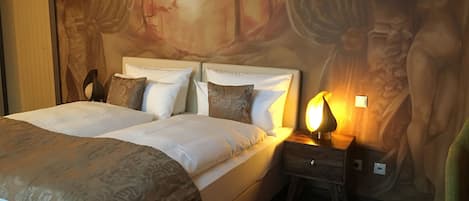 A double bed with a headboard, a bedside table with a lamp, and a mural on the wall.