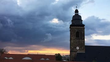 A tower with a clock, surrounded by buildings with red roofs, under a cloudy sky.