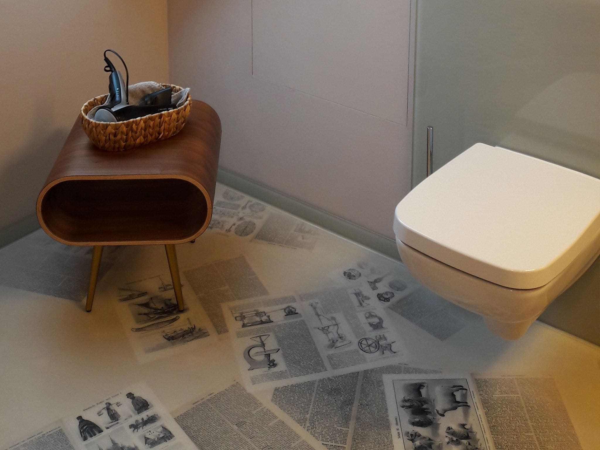 Un baño con tocador de madera, un inodoro blanco y un suelo cubierto de recortes de periódico.