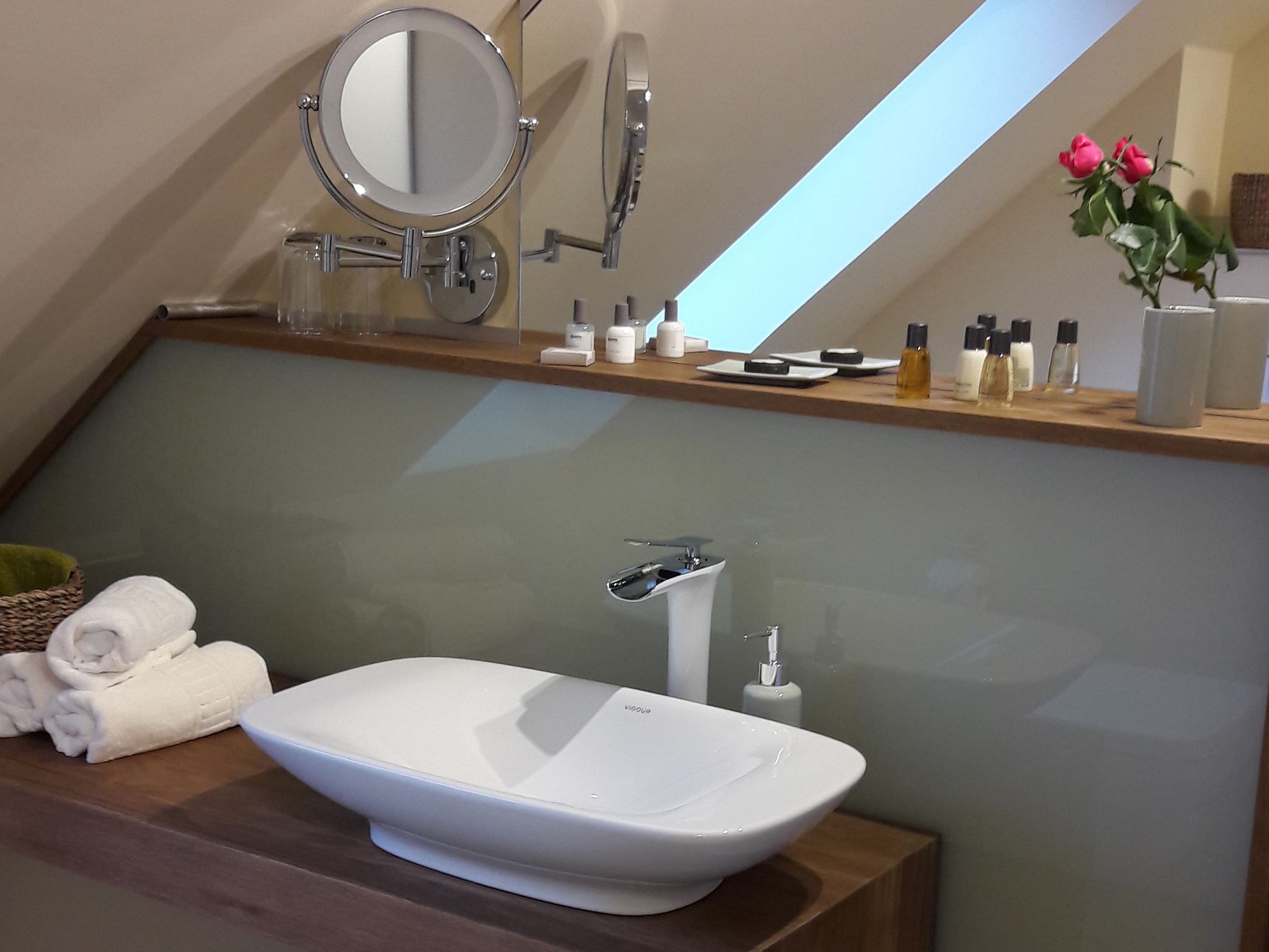 Un baño moderno con un lavabo ovalado grande, un espejo y una zona de ducha. Hay toallas y artículos de aseo en la encimera.