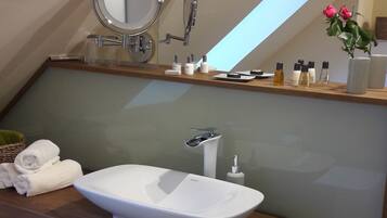 Un baño moderno con un lavabo ovalado grande, un espejo y una zona de ducha. Hay toallas y artículos de aseo en la encimera.