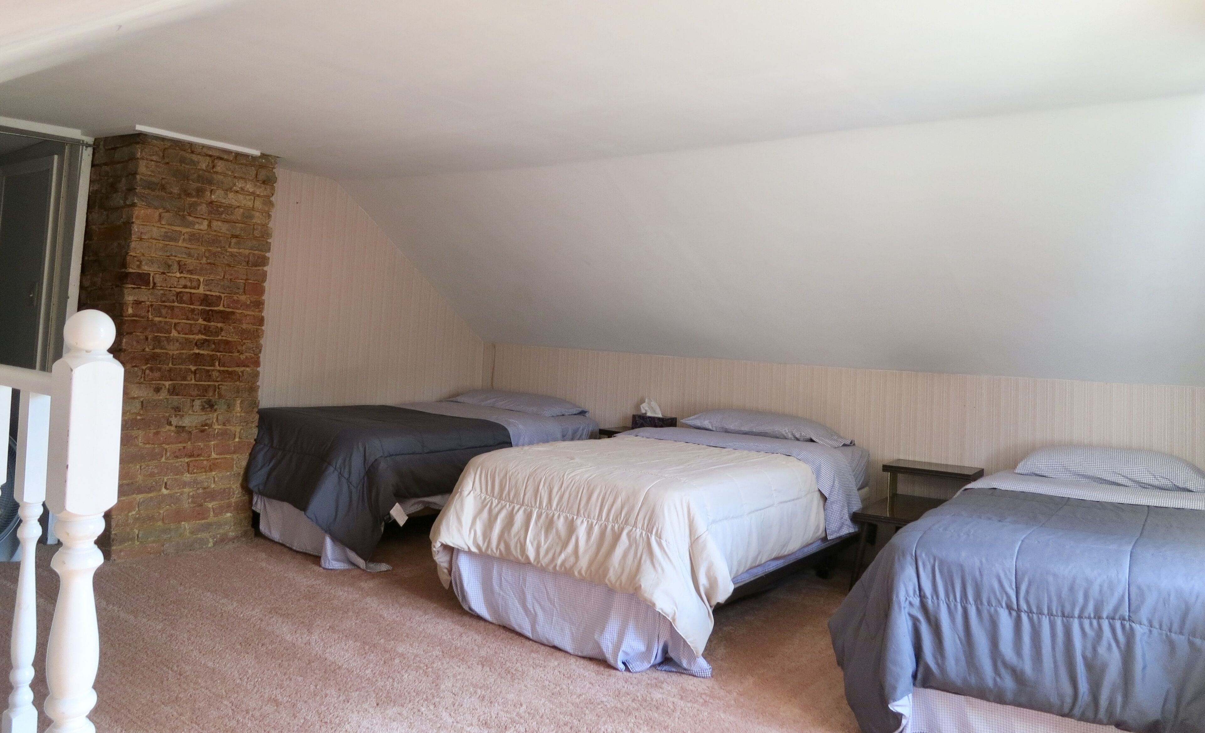 A room with three beds arranged in a row against a brick wall and a sloped ceiling.