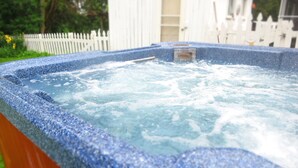 A hot tub with a stone exterior, surrounded by a wooden deck and a white fence. - The Homestead, at Nine Pines Farm - Hot Tub and Walking Trails (Nelsonville)