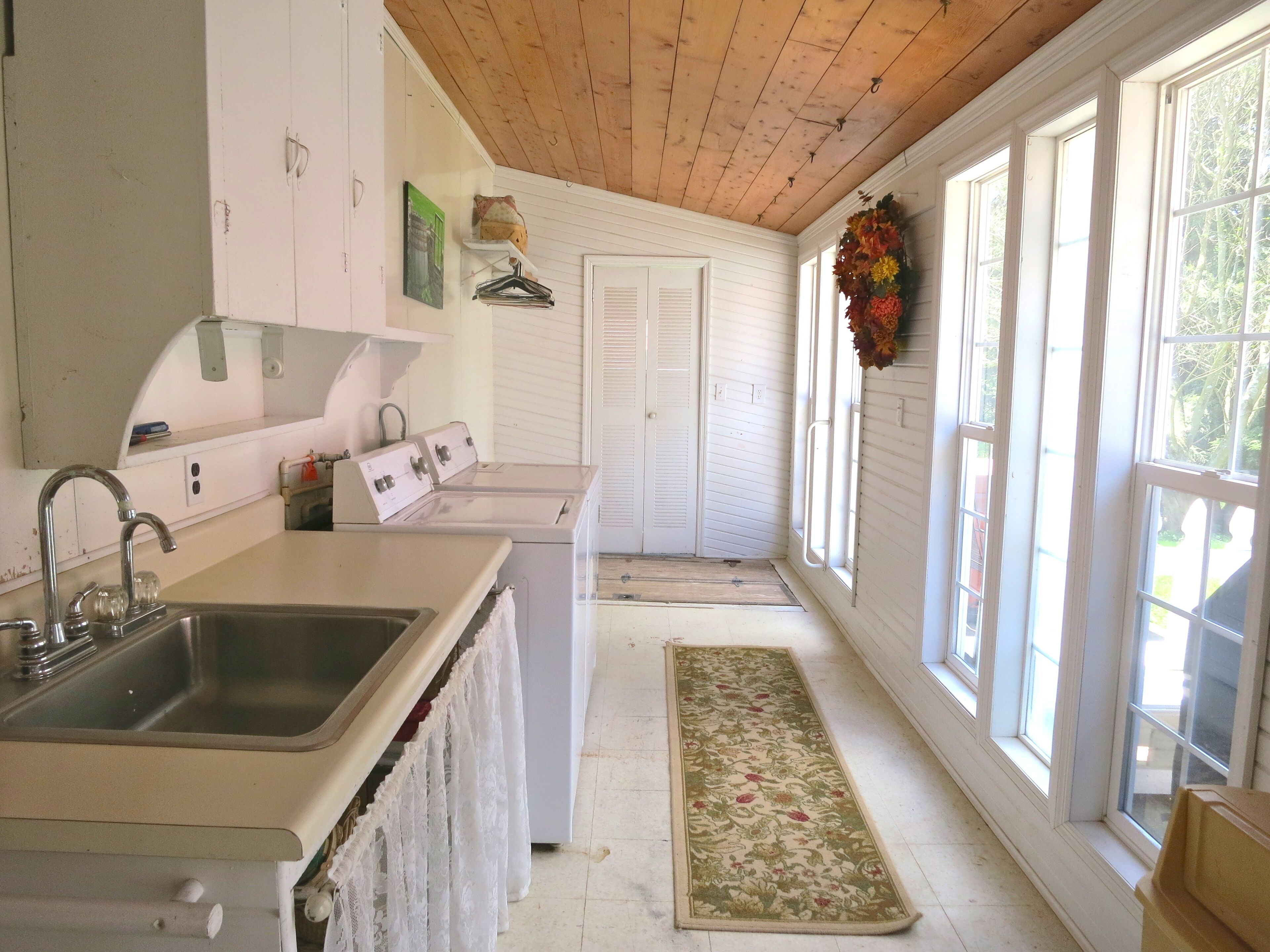 A kitchen with a sink, stove, and white cabinets. There is a door leading to another room and a window with a view of trees.