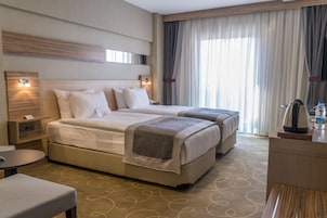 A hotel room with two beds, a desk, a chair, a nightstand, and a large window with curtains.