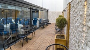 An outdoor patio area with tables and chairs, a stone wall, and a small potted plant. - Greymark Hotel (Izmir)