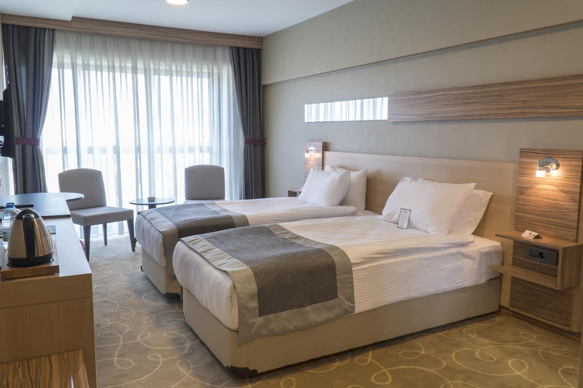 Quarto de hotel com duas camas, uma escrivaninha, uma cadeira e uma televisão.