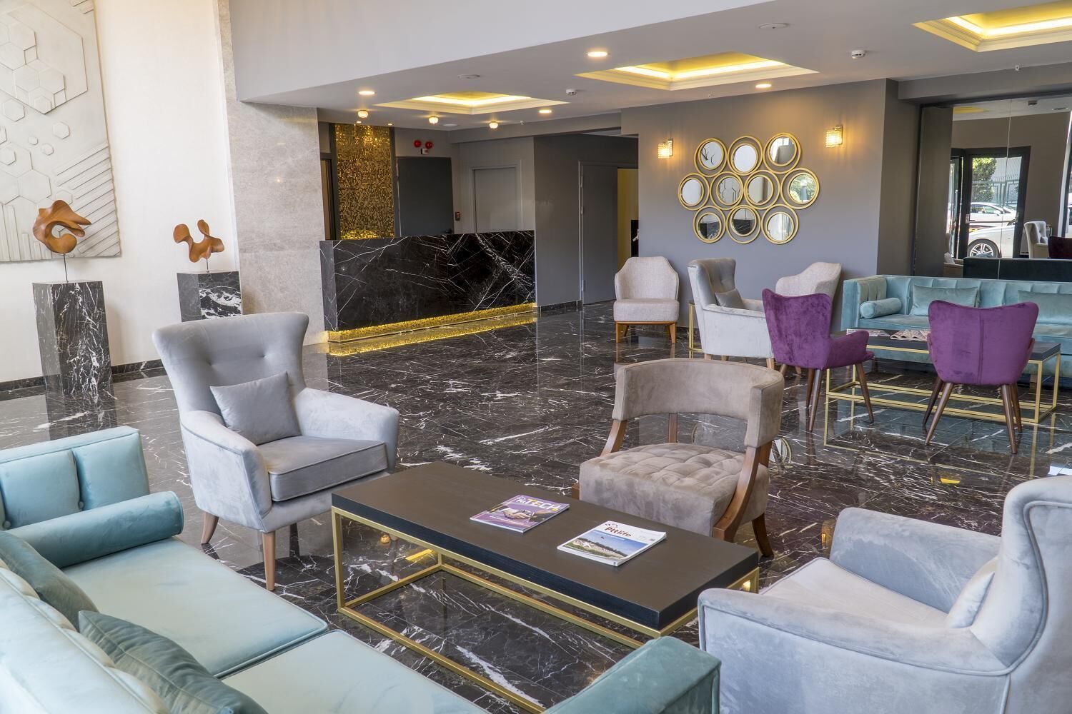 Eine Lobby mit Marmorboden, moderner Sitzgelegenheiten, einem Empfangstisch und einer Wand mit runden Spiegeln.
