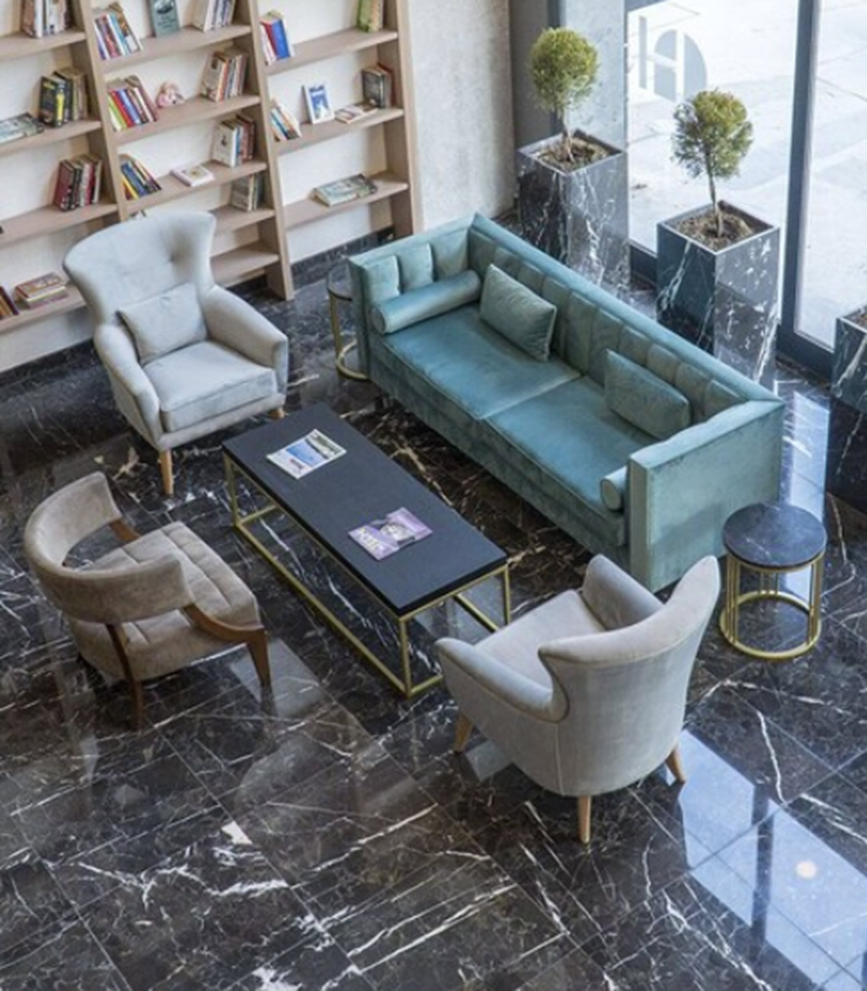 A modern living room with a teal sofa, two armchairs, a coffee table, and a bookshelf filled with books.