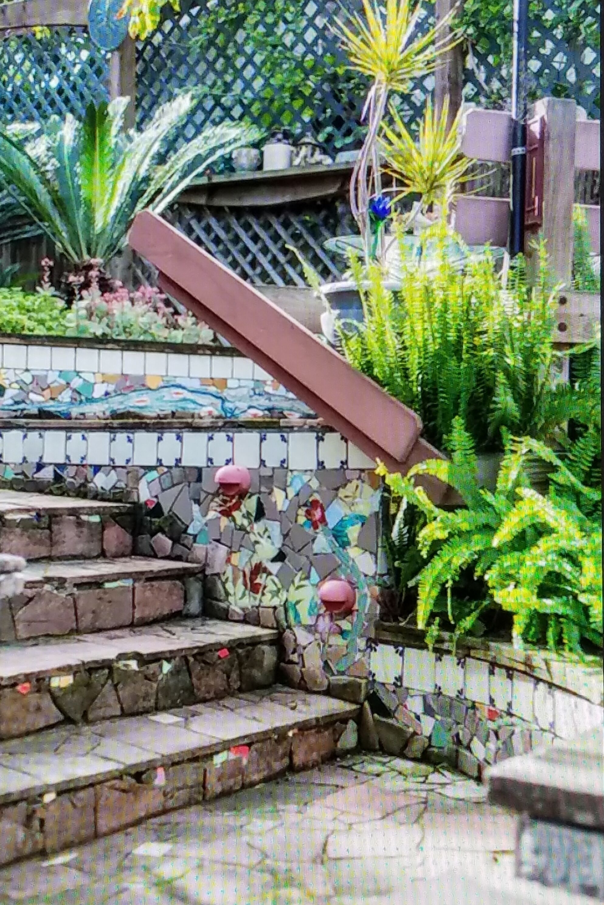 Una escalera con diseño de mosaicos, rodeada de plantas y una valla de madera.