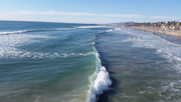 Une plage avec des vagues, un rivage sablonneux et une vue lointaine sur la ville.