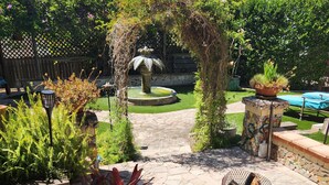 Un sentier de jardin menant à une fontaine, entourée de plantes en pot et d’un bassin.