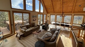 Amplia sala de estar con techo alto y ventanas grandes, piso de madera y una zona de estar acogedora.