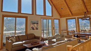 Amplia sala de estar con ventanas grandes, techo de madera y vistas a un paisaje nevado.