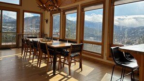 Un comedor con mesa y sillas de madera, ventanas amplias con vistas a las montañas y un candelabro.