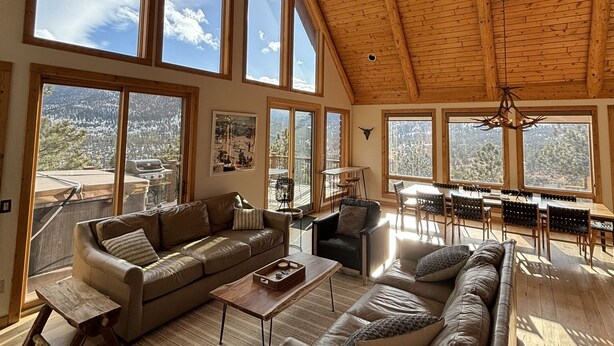 Amplia sala de estar con ventanas grandes, techo alto con vigas de madera y comedor con vistas a las montañas.