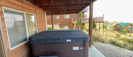 A hot tub outside a wooden cabin with a covered porch, steps leading up to it, and a view of neighboring houses.