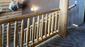 Una escalera de madera con barandilla, un aplique de pared y una cabeza de venado montada.