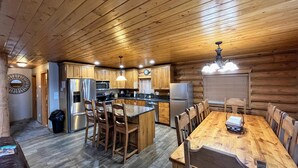 Interior de una cabaña de madera con cocina, comedor y una gran mesa de madera con sillas.
