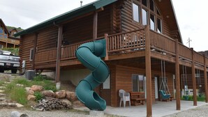 Una cabaña de troncos con fachada de madera, un balcón y un tobogán espiral verde.