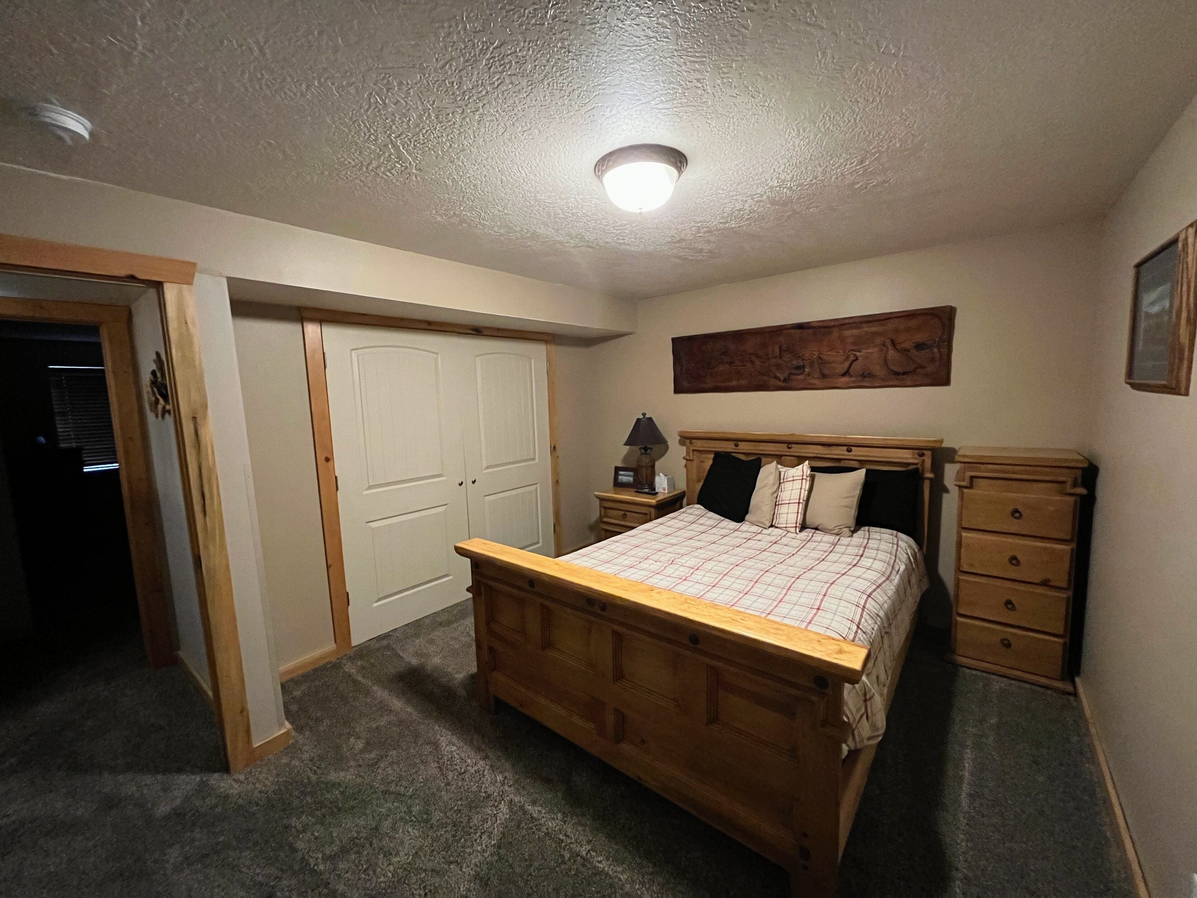 A bedroom with a wooden bed, a nightstand, a dresser, and a door leading to another room.