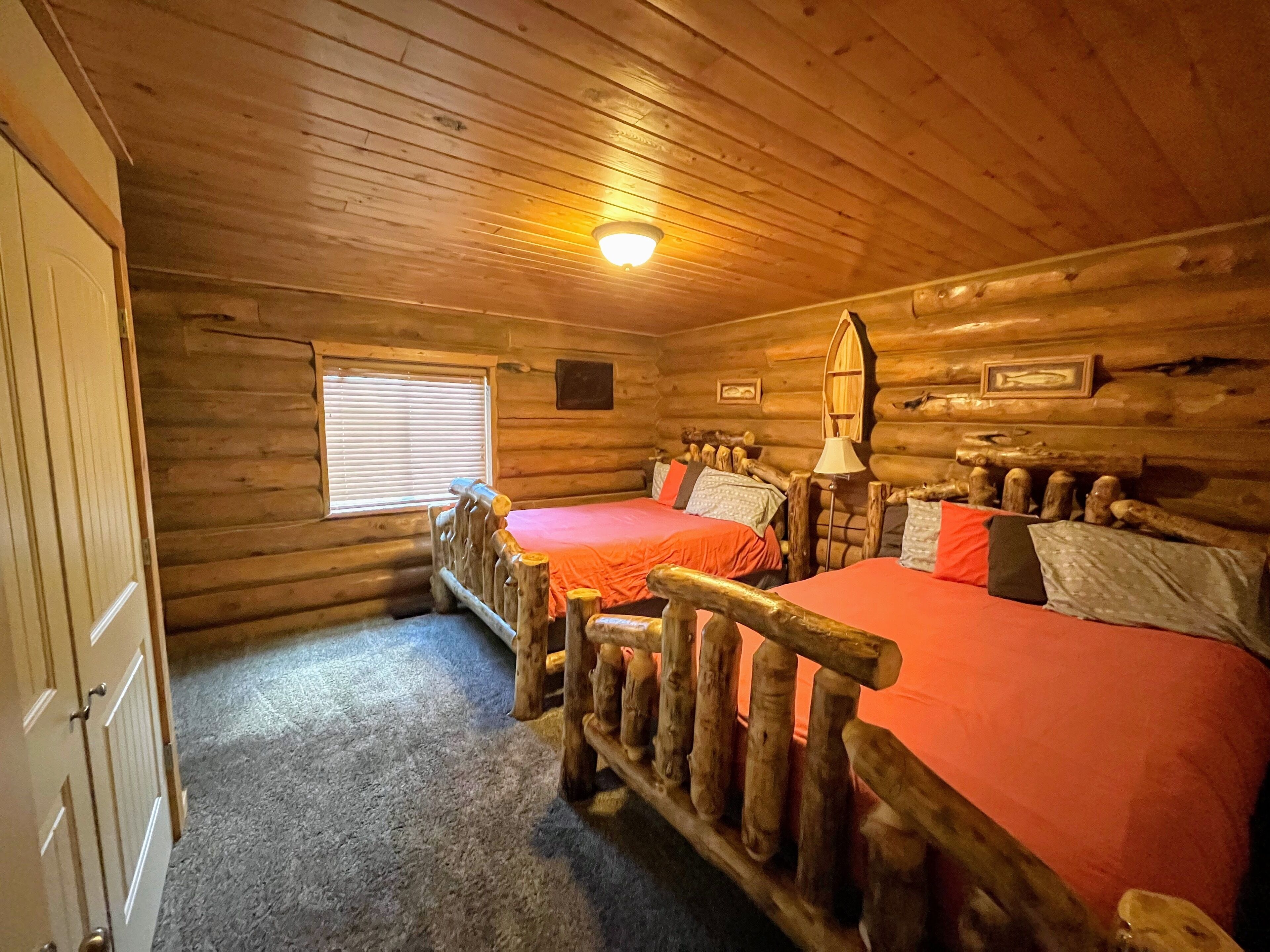 Une chambre de style rustique avec deux lits, une tête de lit en bois, une fenêtre avec des stores et une porte.