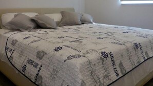 Une chambre à coucher comprenant un lit, des oreillers, une couverture à motifs marins, un appareil de climatisation et une fenêtre avec des stores.