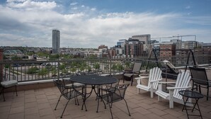 A rooftop terrace with a table and chairs, offering a view of the city skyline.