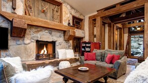 A cozy living room with a stone fireplace, wooden beams, and comfortable seating. - Large, Luxe, walk2town, 2 min DV & PC bases. Theater, game room, steam room (Park City)