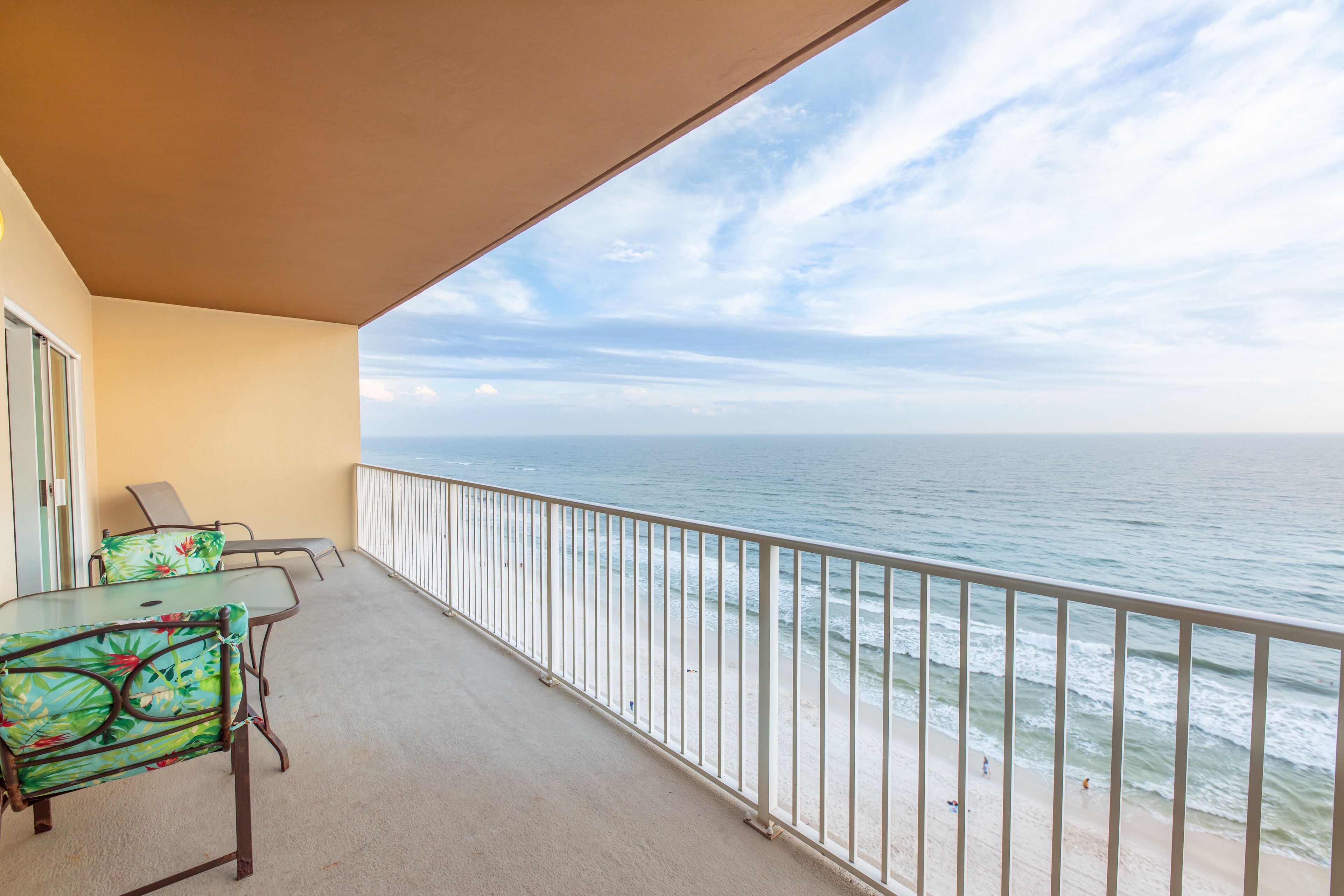A balcony with a view of the ocean, a table with chairs, and a railing.