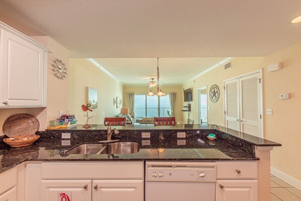 A kitchen with a granite countertop, stainless steel sink, and white cabinetry.