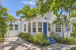 Un bâtiment blanc avec une porte bleue, entouré d’une végétation luxuriante et de palmiers.
