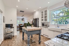 A modern kitchen with white cabinets, a wooden island, and a large window with a view of greenery.