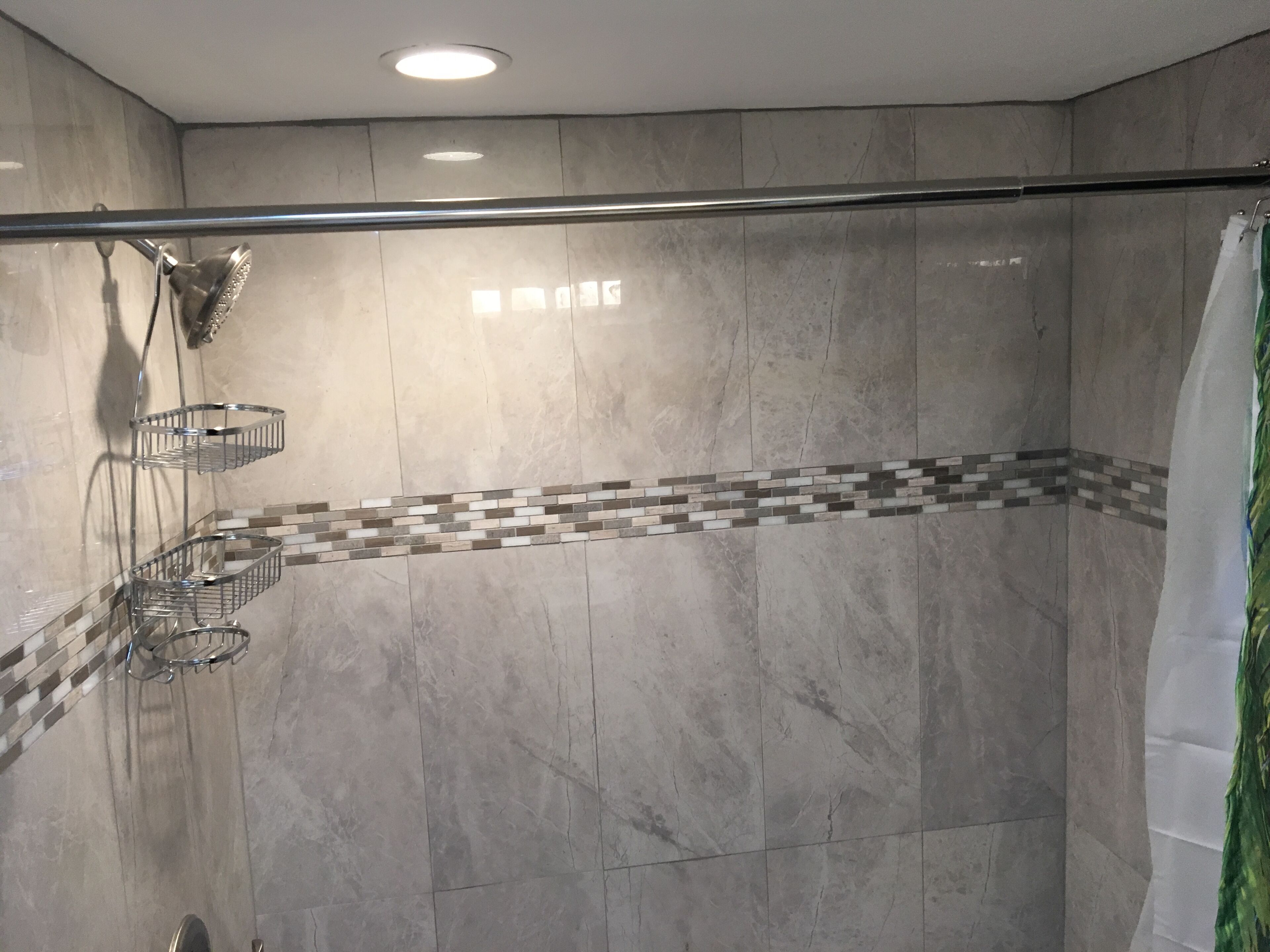 Douchegedeelte met een glazen wand, een metalen rek en een betegelde spatwand.