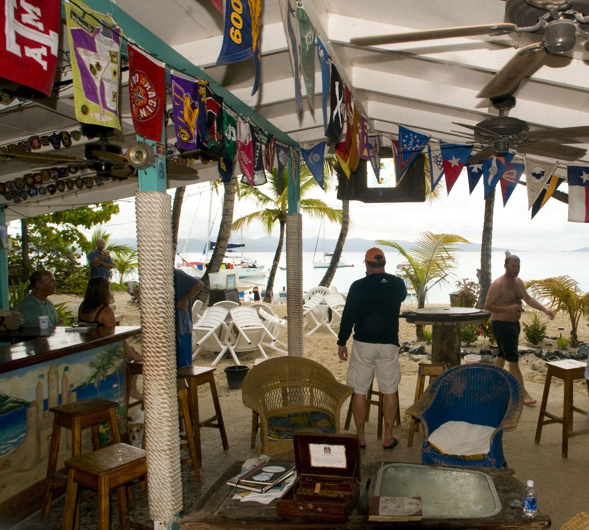 Un bar situé en bord de mer, doté d’une terrasse, d’un ventilateur de plafond et de divers drapeaux.