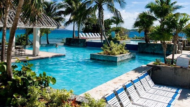 A pool area with lounge chairs, palm trees, and a view of the ocean.