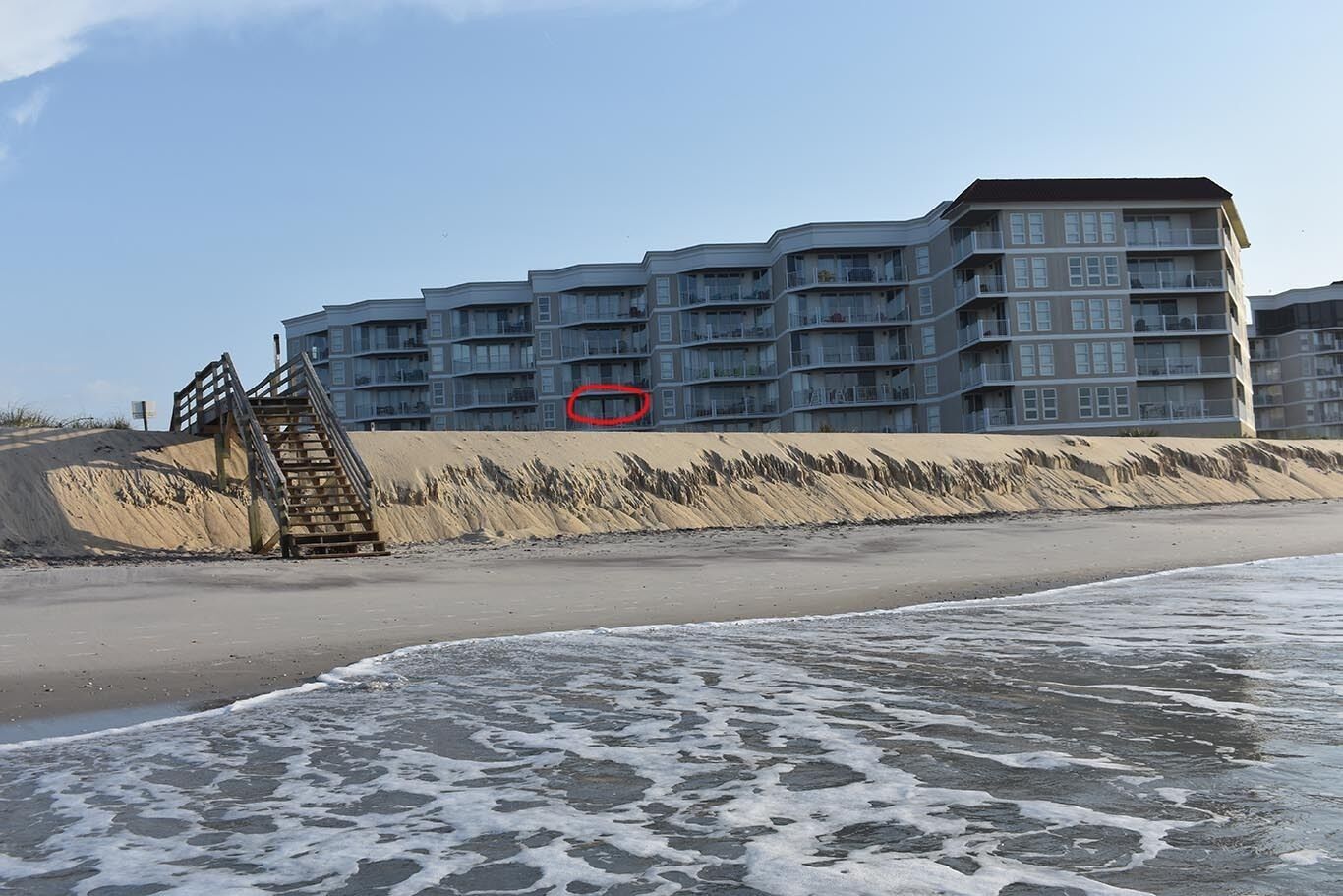 Ein Strandhotel mit mehreren Balkonen, einem Sandstrand und einer Holztreppe zum Strand.